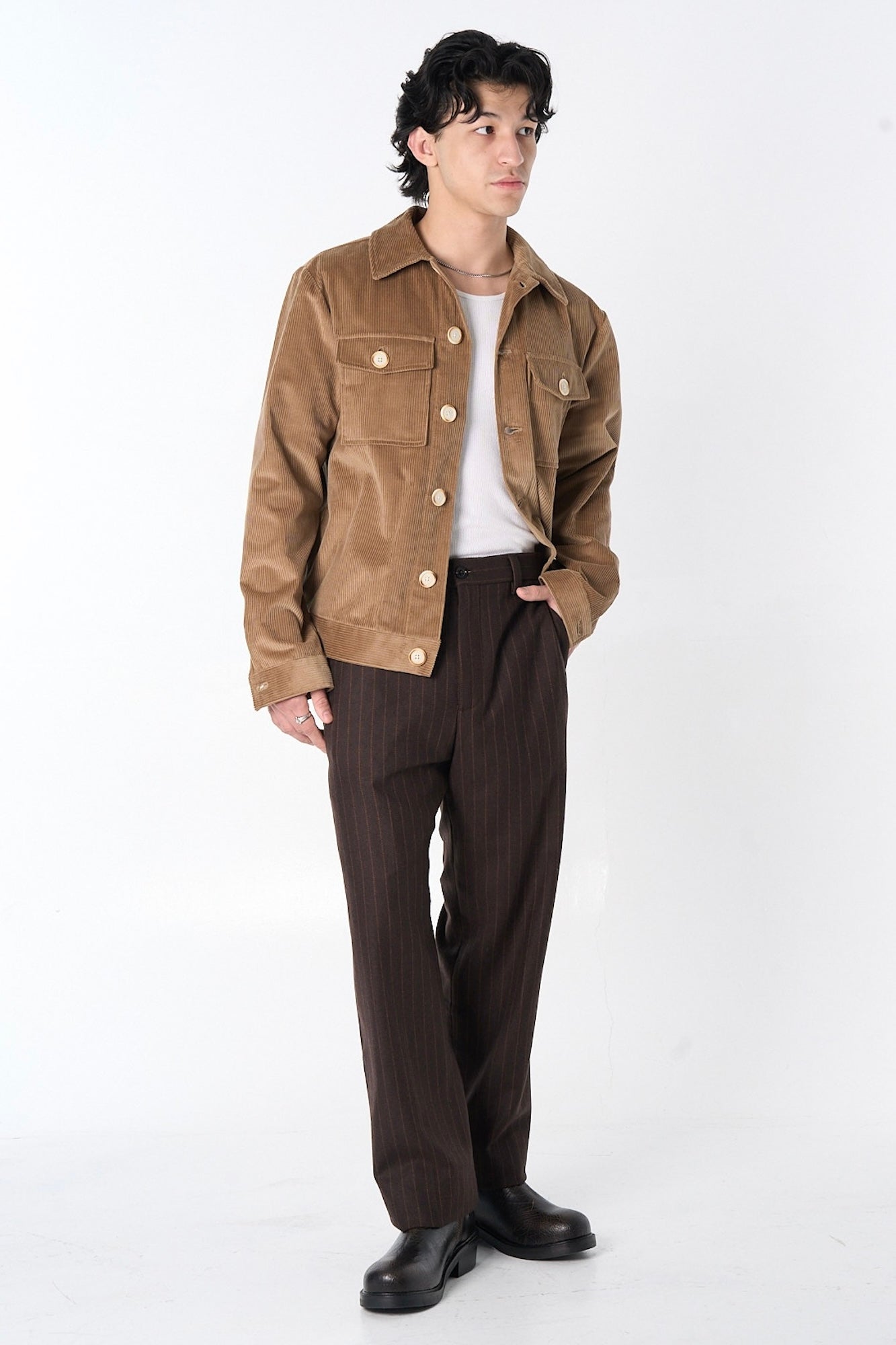 Man wearing a brown corduroy jacket with a white tank top and brown striped pants