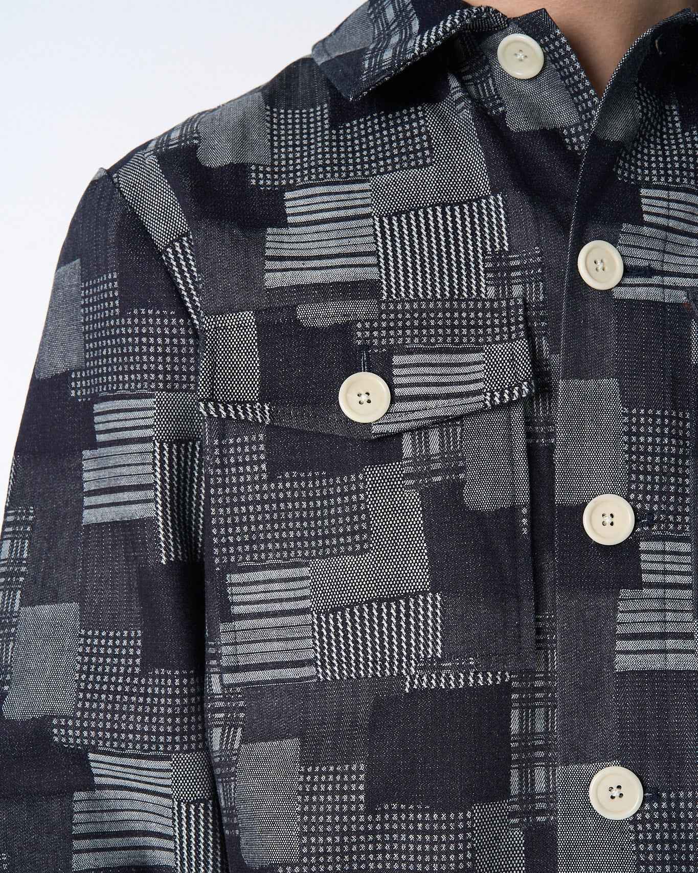 Dean Jacket in dark denim patchwork jacquard with relaxed boxy fit, shown on model from chest up displaying intricate woven texture and natural corozo buttons.