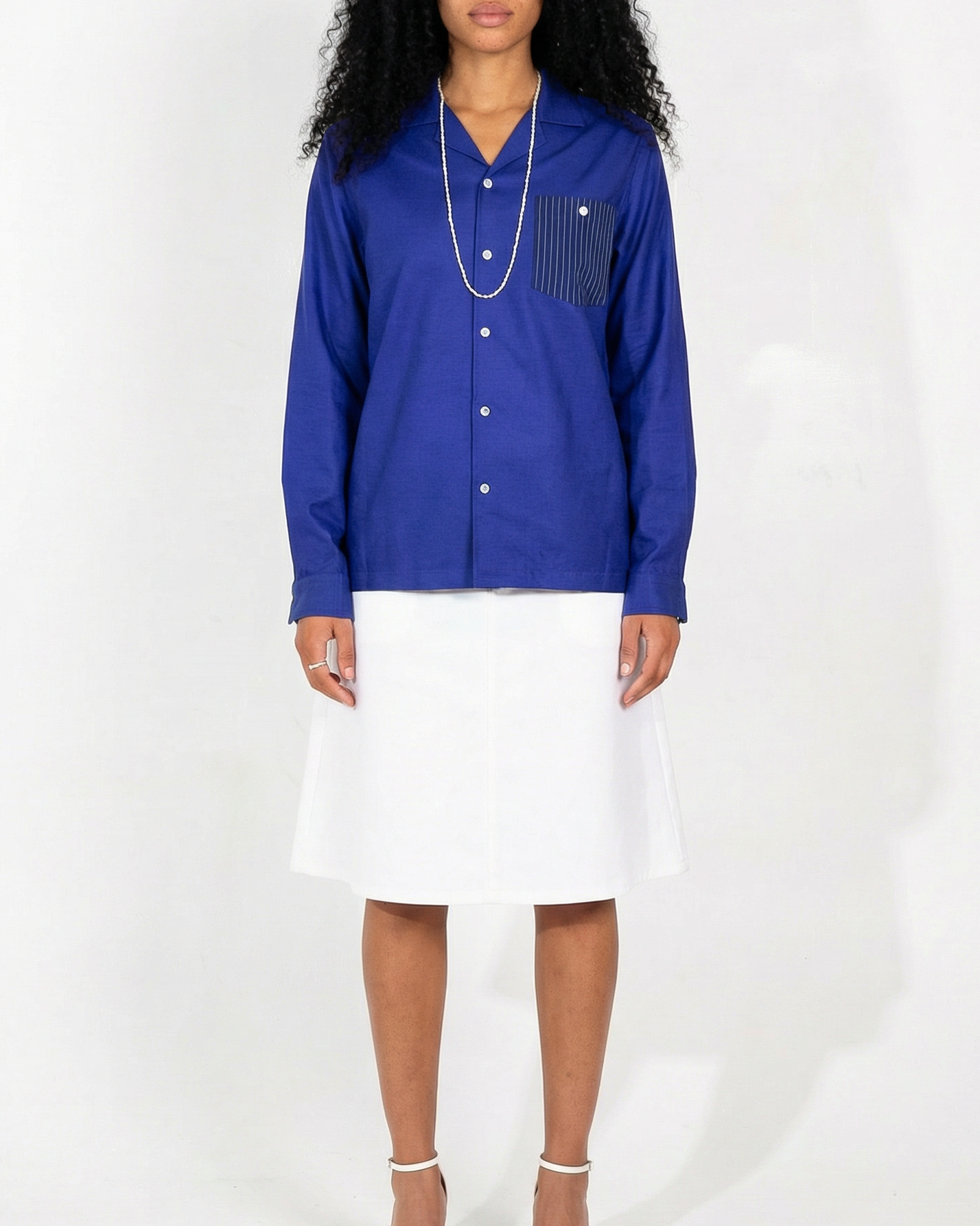 Arenas convertible-collar shirt in royal blue and white stripe cotton cupro linen, relaxed fit, worn by woman with long curly black hair and silver jewelry.