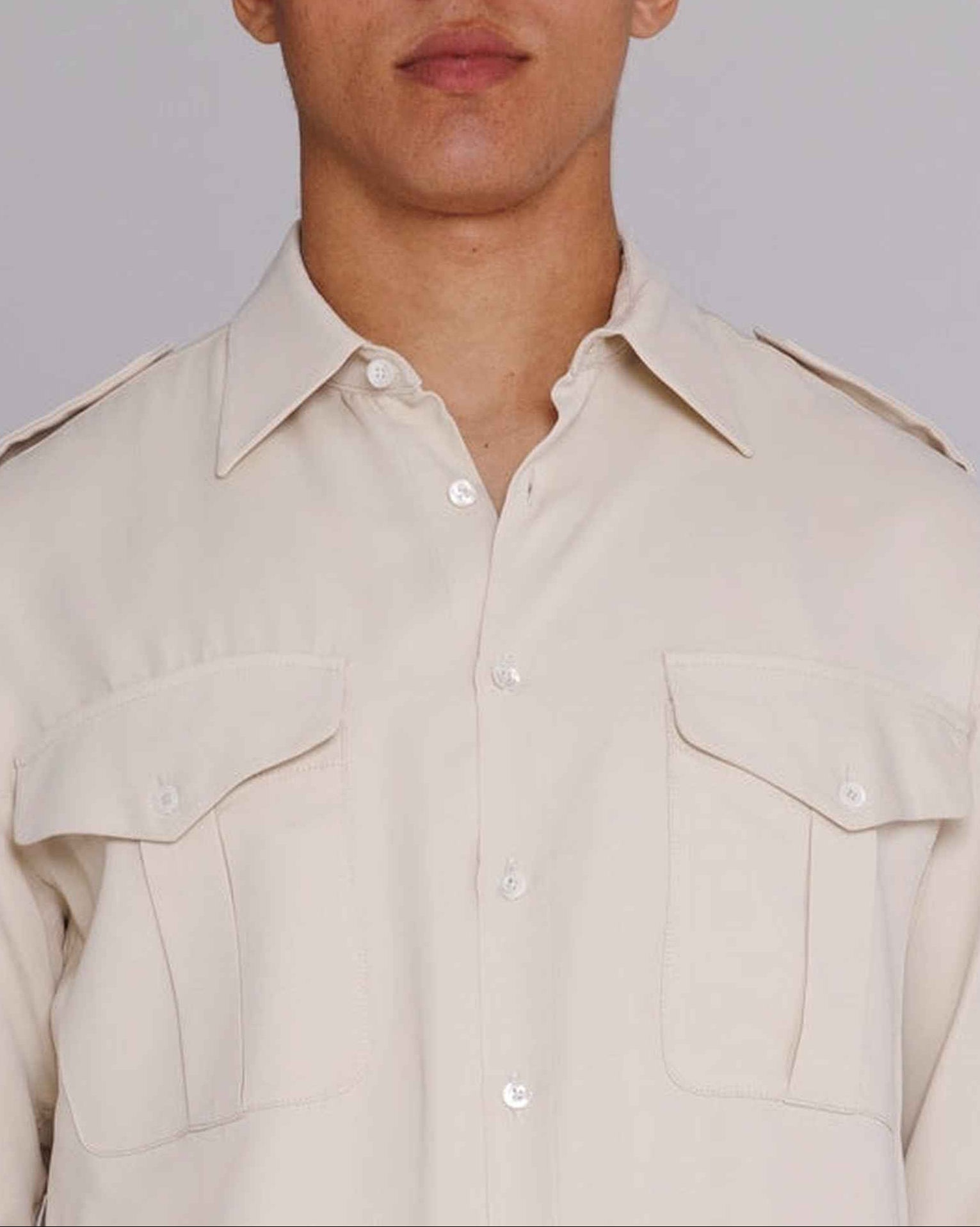 Model wearing natural satin Jones Safari Shirt with spread collar, chest pockets, and shoulder epaulets, shown in three-quarter view.