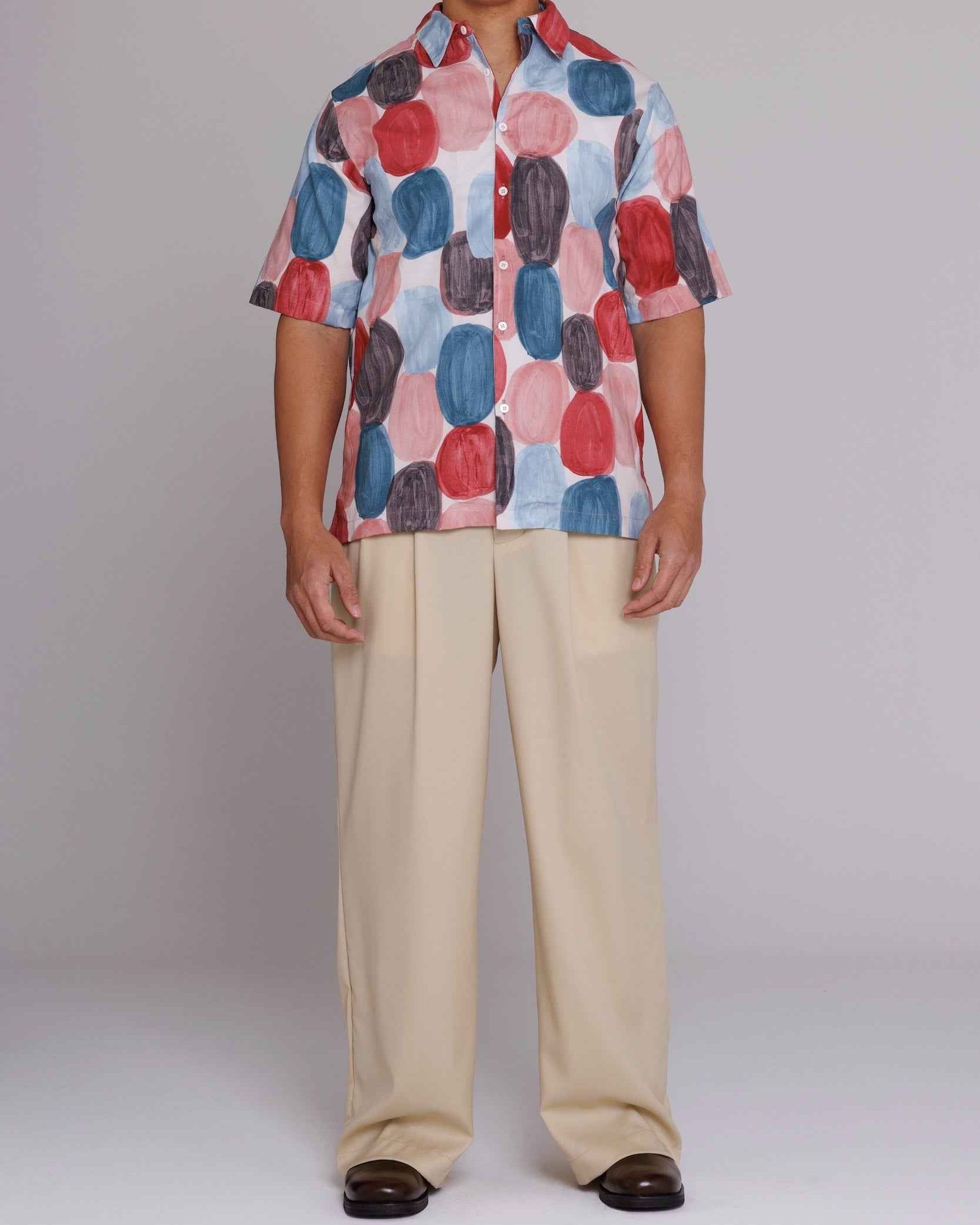 Flowers" button-up shirt in red, blue, and black dot print on model, loose fit, cotton poplin, side seam openings visible.