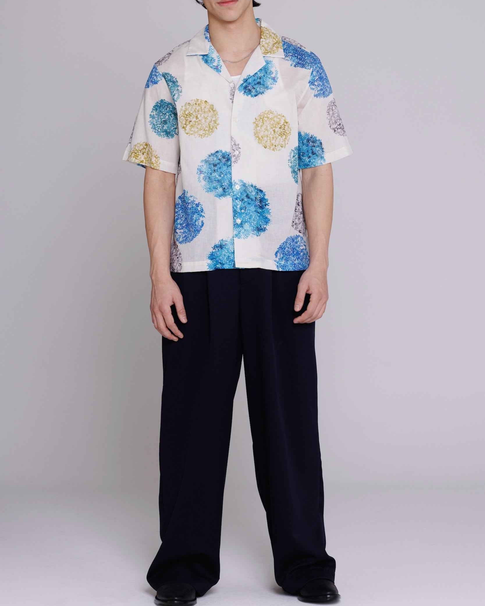 Arnaz Resort Shirt in blue and gold watercolor leaves print, cropped fit, worn by model with arms at sides showing side seam openings and back pleating detail.