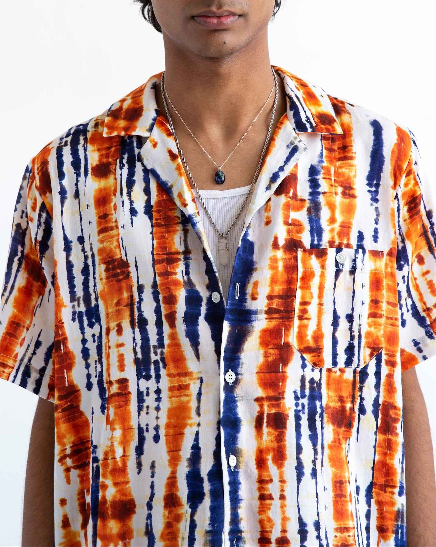 Desi short sleeve resort shirt in blue and orange batik print, Cuban collar, relaxed fit with side slits, modeled on person.