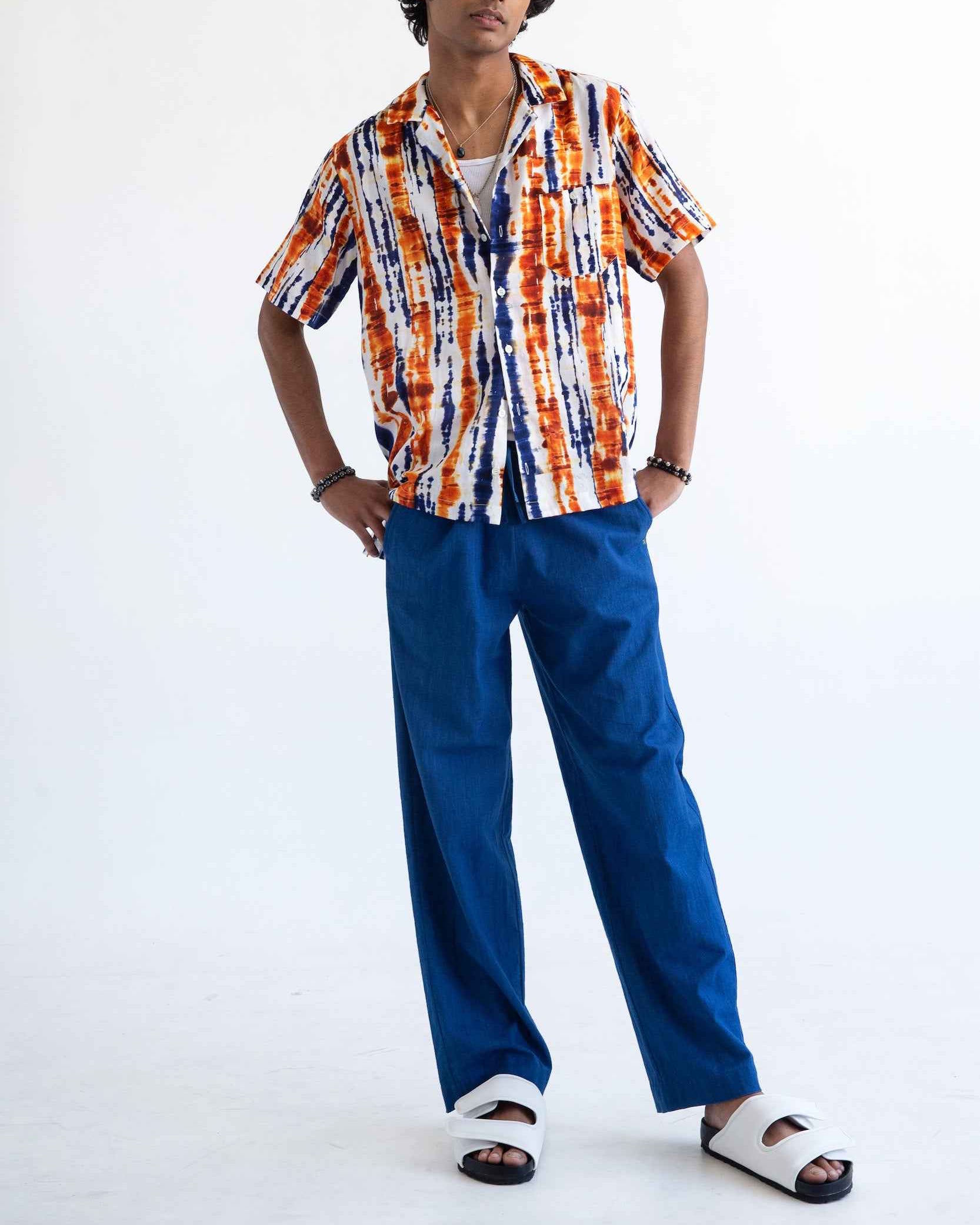 Desi short sleeve resort shirt in blue and orange batik print, Cuban collar, relaxed fit with side slits, worn by model.