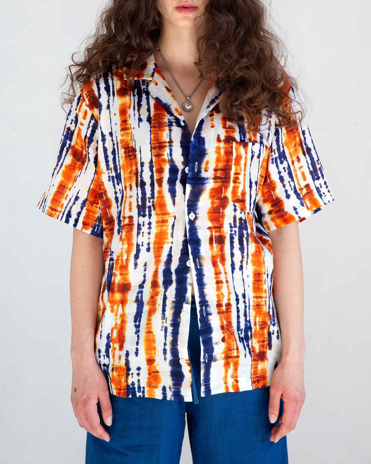 Desi short sleeve resort shirt in blue and orange batik print with Cuban collar, shown on model against neutral background.