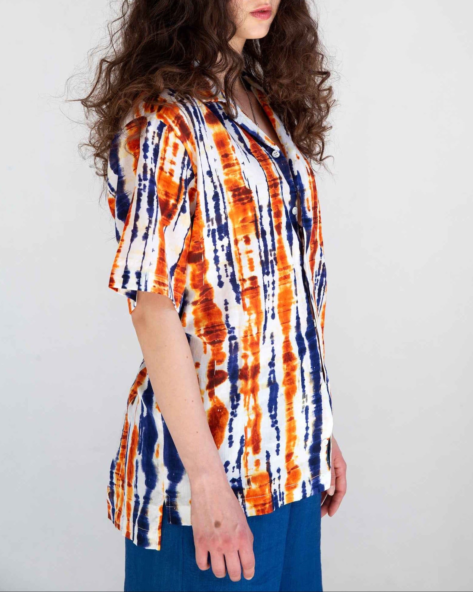 Desi short sleeve resort shirt in blue and orange batik print with Cuban collar, displayed on model showing relaxed fit with side slits.