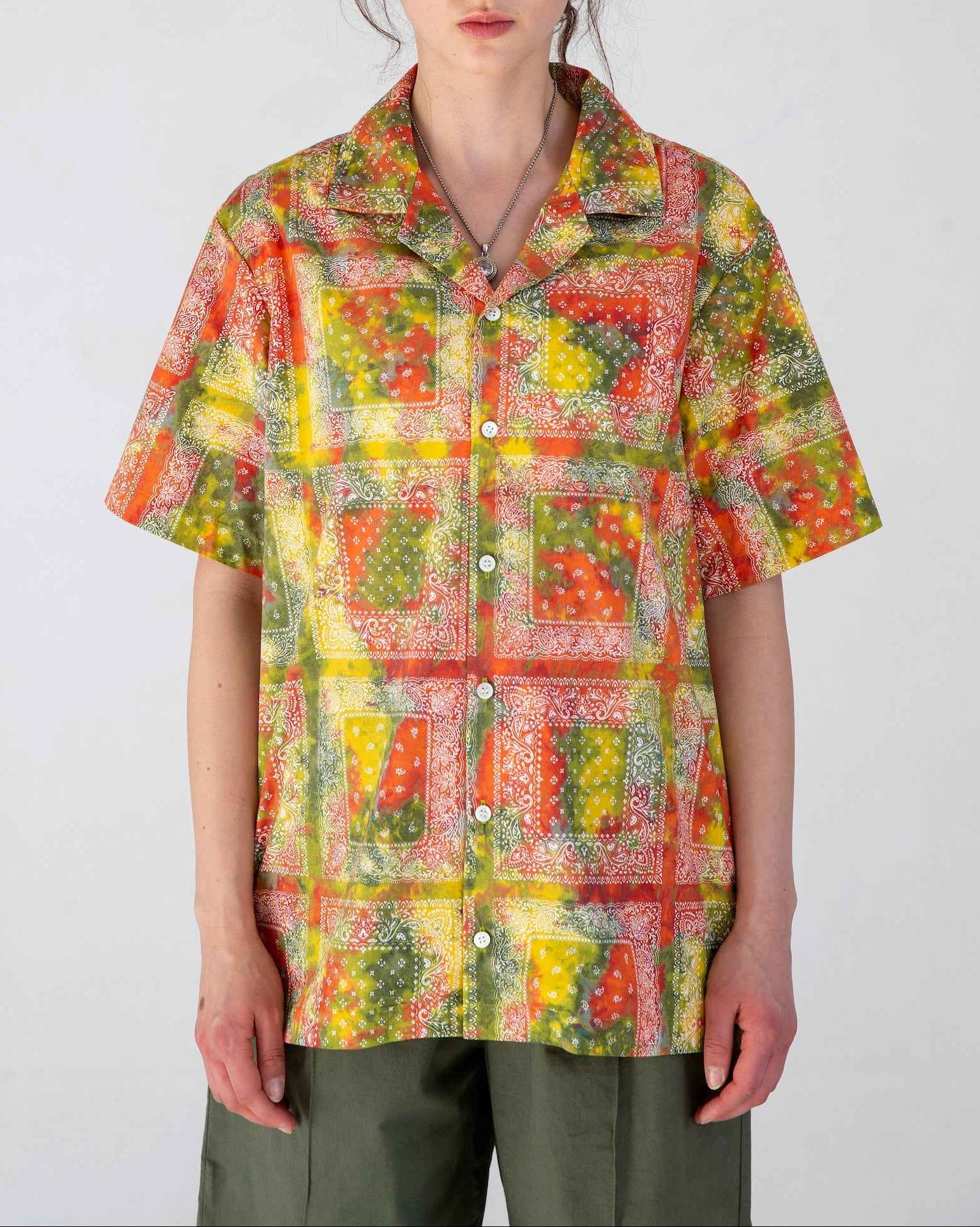 Desi short sleeve resort shirt in red batik bandana print, Cuban collar, organic cotton poplin, relaxed fit with side slits, worn by model.