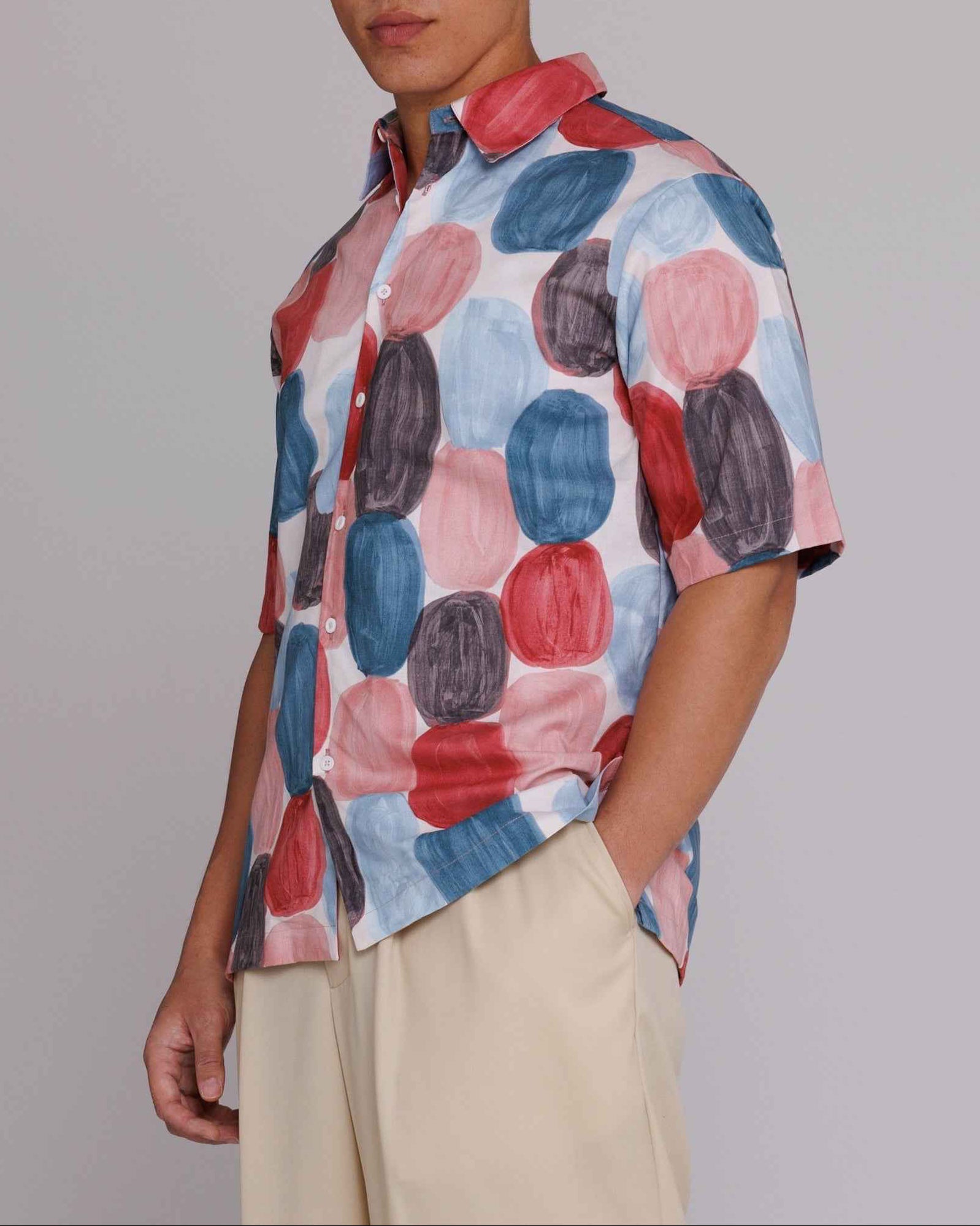 Flowers" button-up shirt in red, blue, and black dot print on model, loose fit, cotton poplin, side seam openings, back pleating