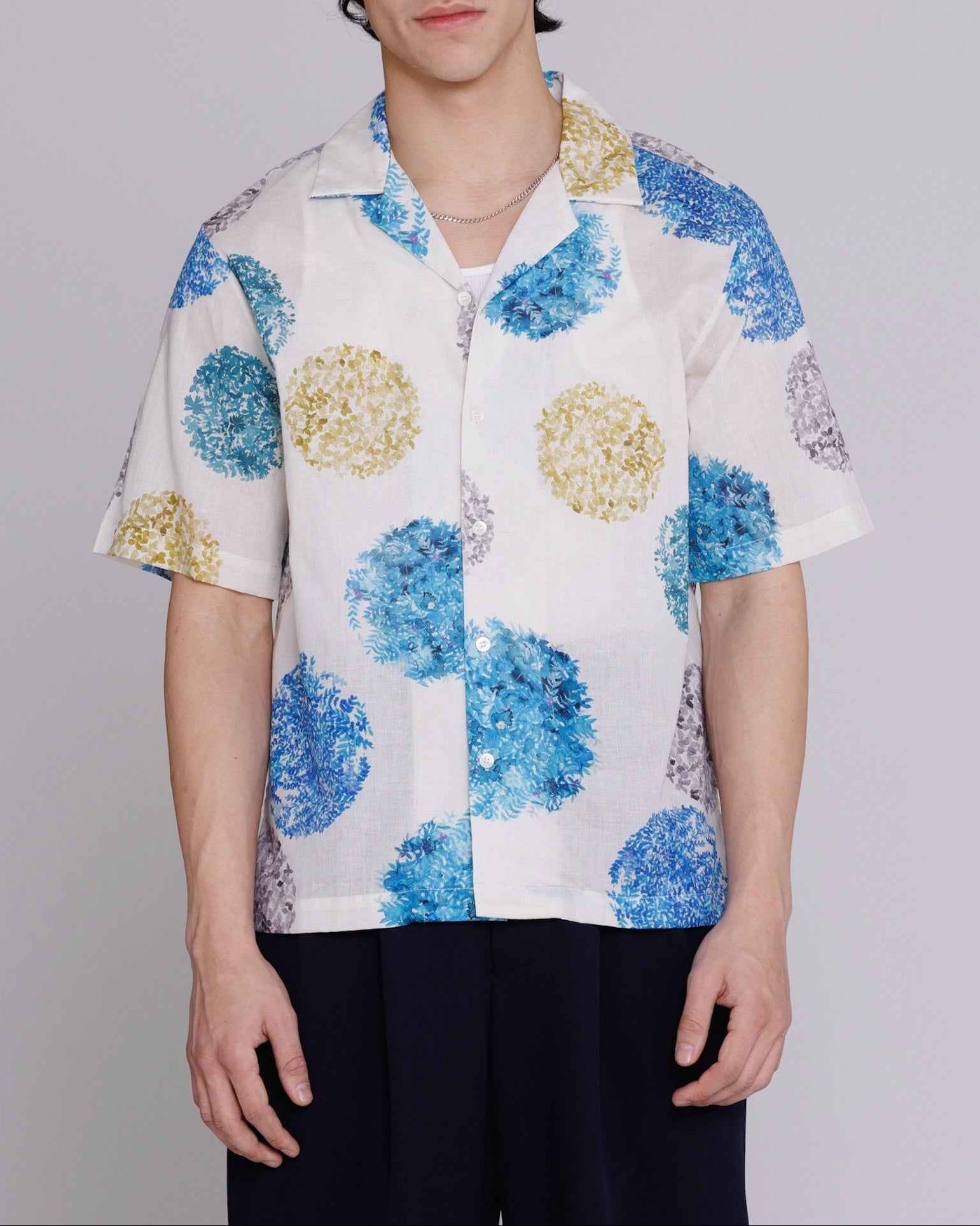Arnaz Resort Shirt in blue and gold watercolor leaves print, cropped fit, worn by model in front pose showing side seam openings and back pleating detail.