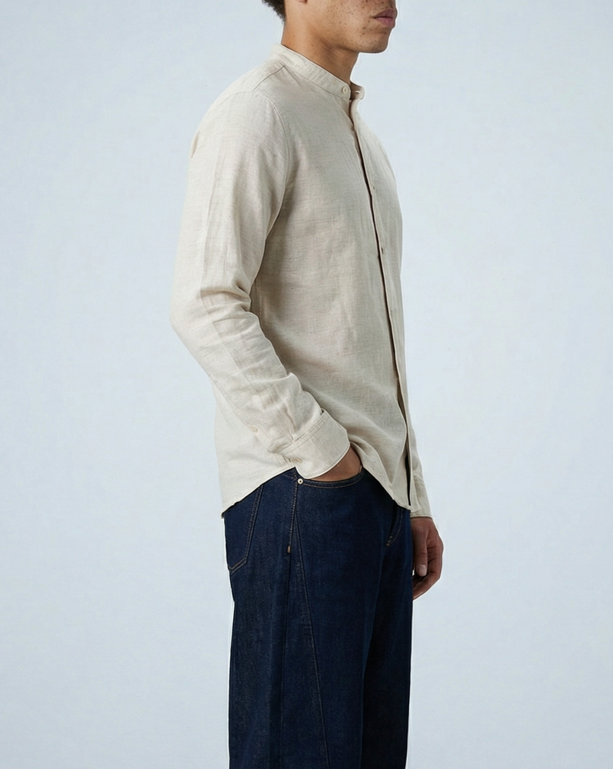 Model wearing Liam band collar vintage cream linen cotton shirt untucked, posed at side angle with hand in pocket, showing relaxed fit through body.