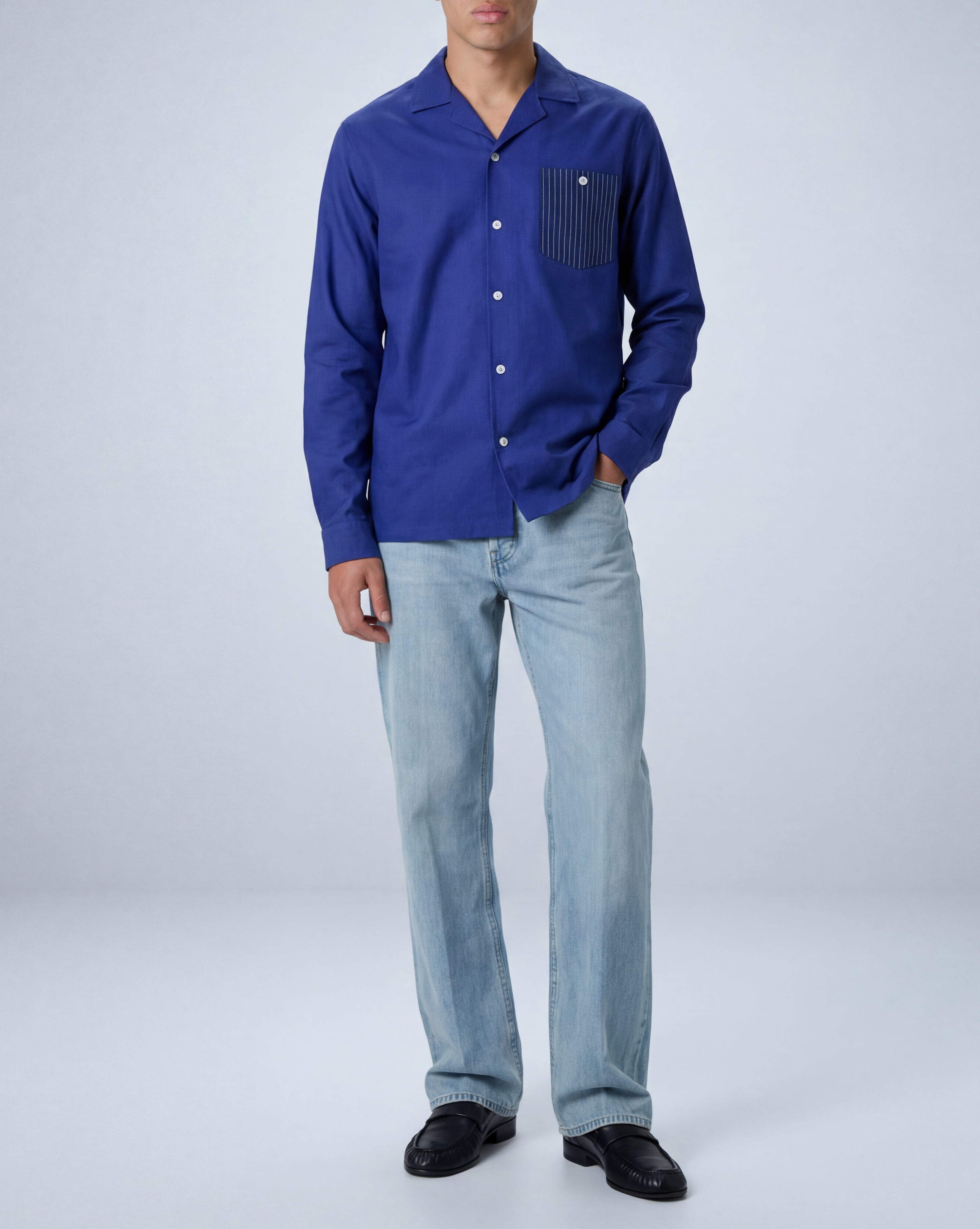 Model wearing Arenas convertible-collar shirt in royal blue and white stripe cotton cupro linen, untucked in relaxed fit, standing in full-length studio shot facing forward.