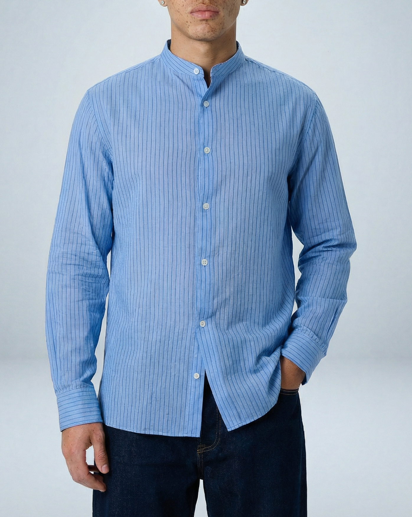 Model wearing Liam band collar shirt in light blue and blue stripe, untucked relaxed fit, hand in back pocket, facing forward against studio background.