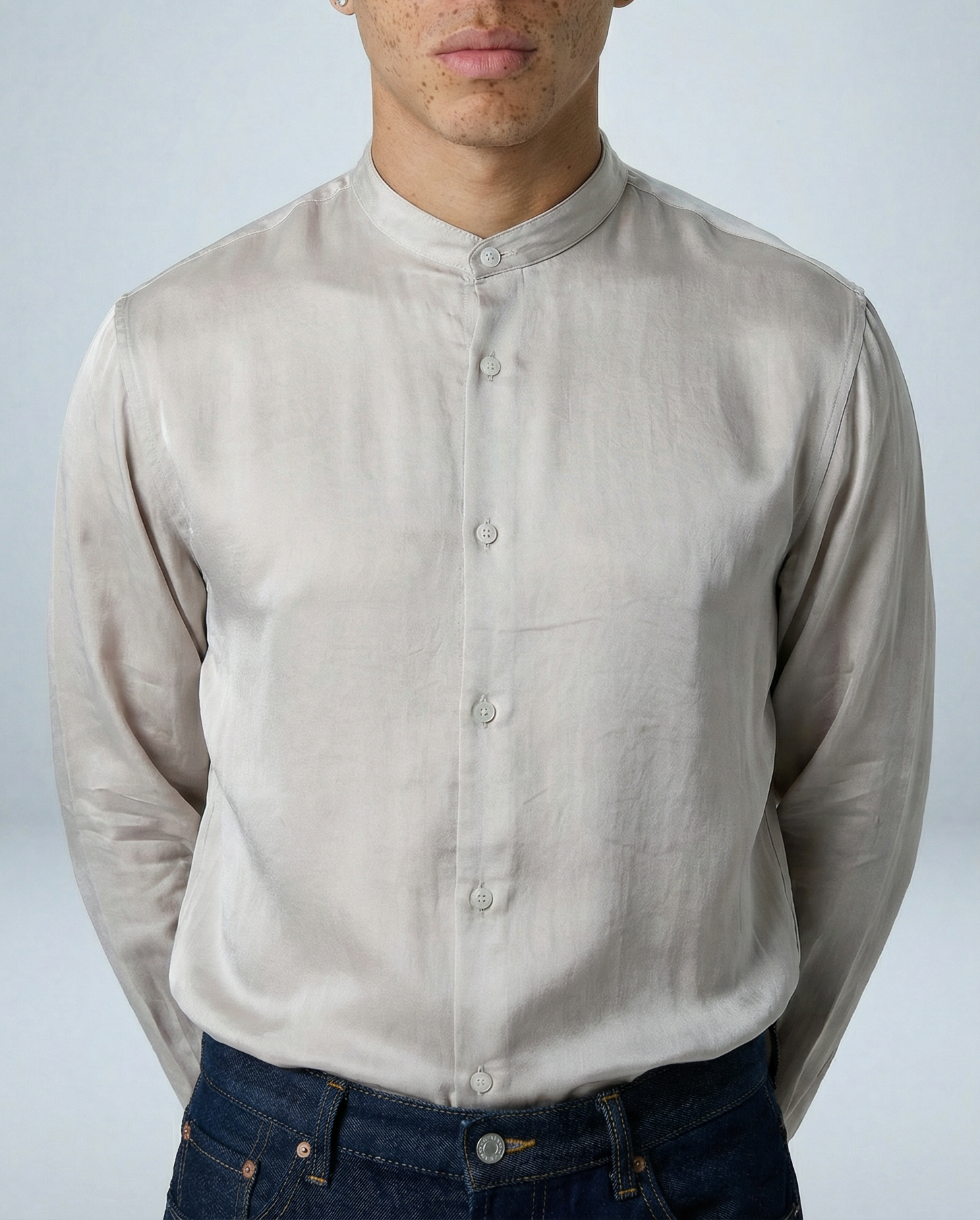 Model wearing Liam band collar shirt in oyster taupe cupro twill, arms behind back, facing forward in studio setting.