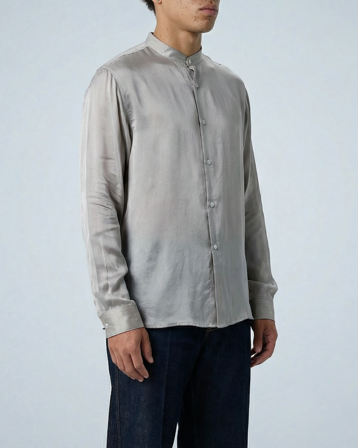 Liam band collar shirt in oyster taupe cupro twill, worn untucked by model standing at slight angle with hands at sides in studio setting.