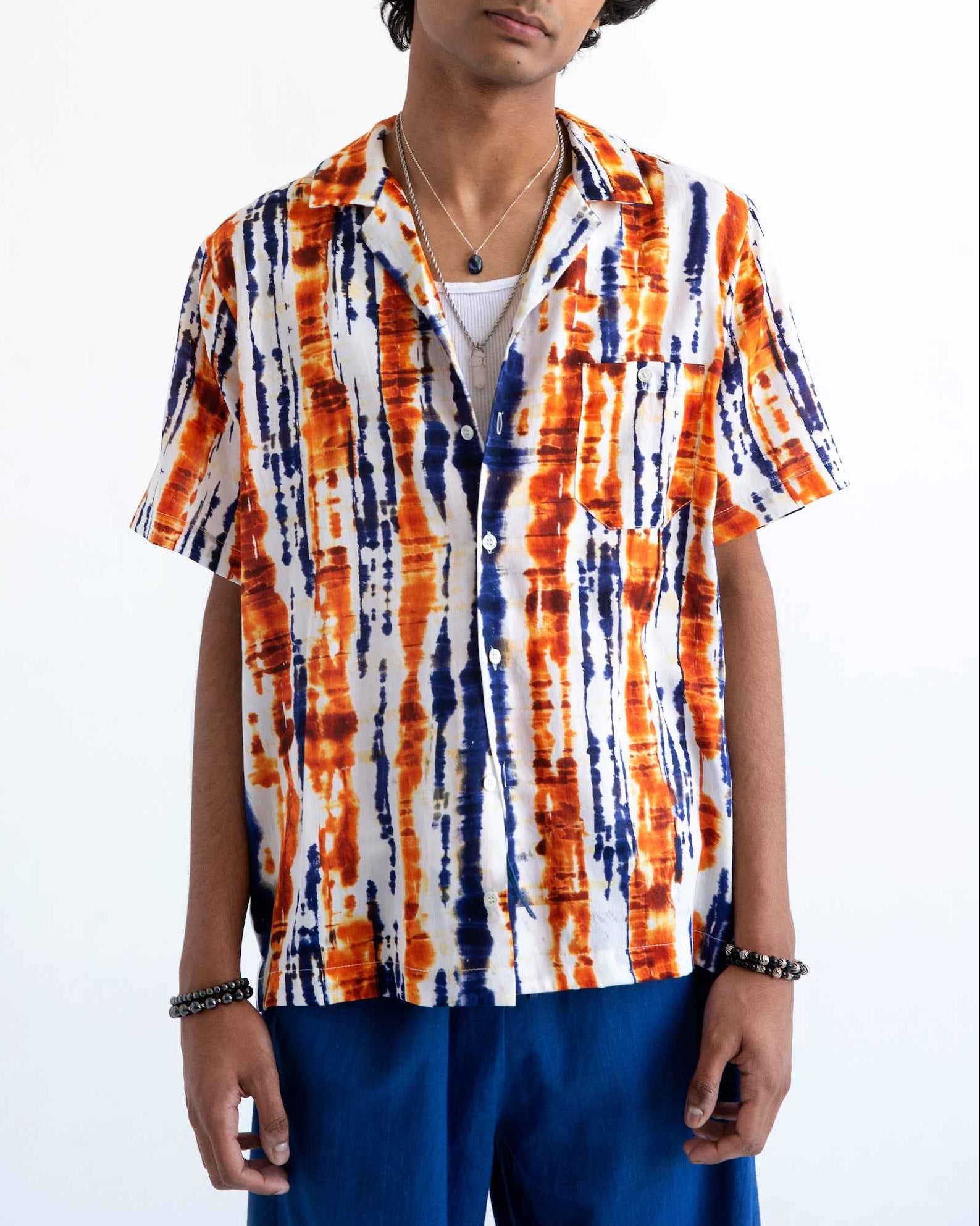 Desi short sleeve resort shirt in blue and orange batik print with Cuban collar, displayed on model in relaxed fit with side slits.
