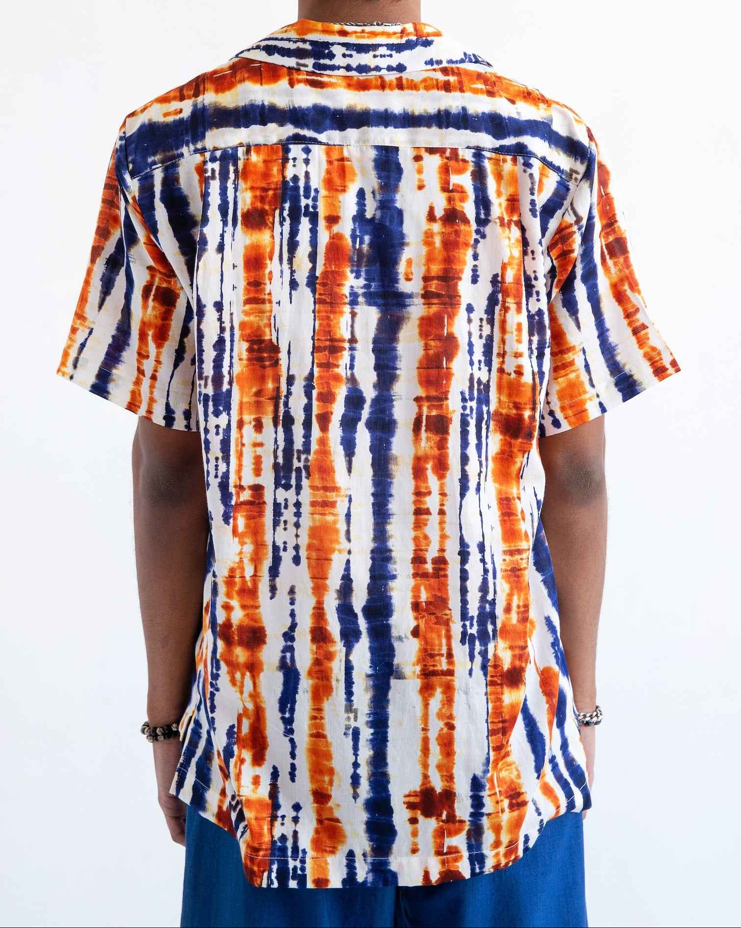 Desi short sleeve resort shirt in blue and orange batik print, Cuban collar, relaxed fit with side slits, worn by model.
